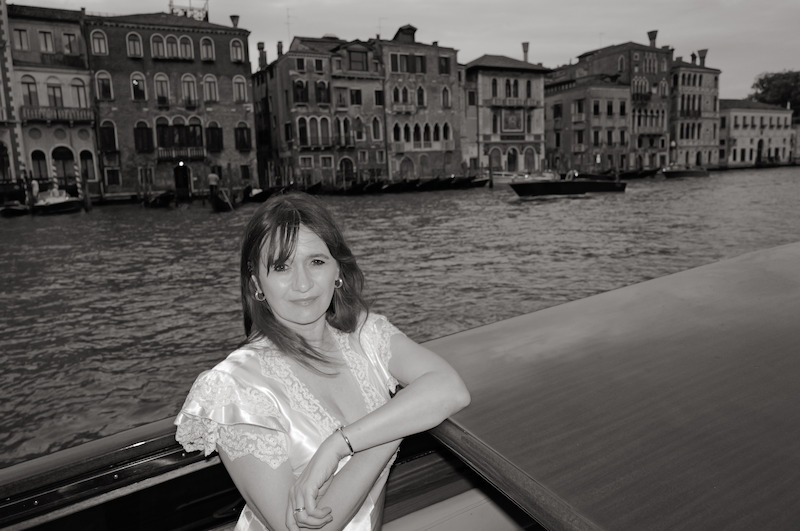 Emily Mortimer, dressed in a silk and lace dress, poses on a boat in Venice.