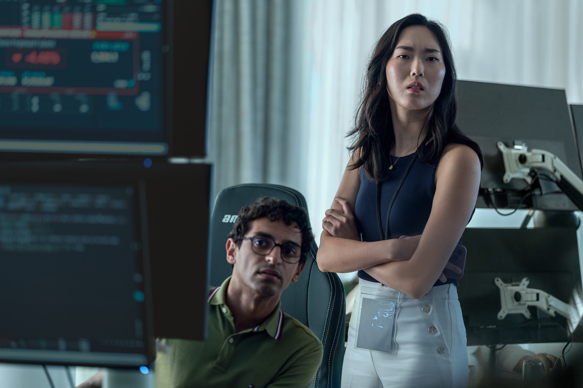 A man and woman in a modern office intently looking at computer screens displaying data, with chairs and equipment visible in the background, suggesting a tech or research environment.