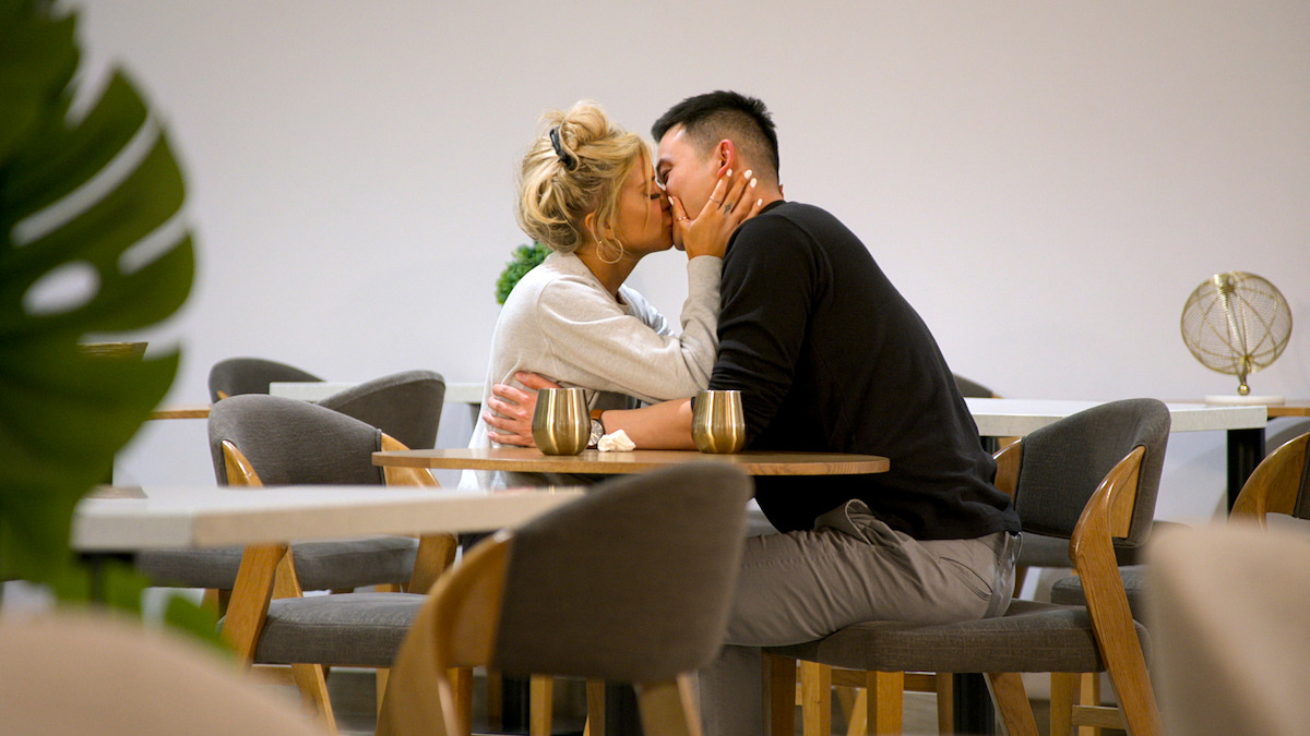 A couple sharing a kiss in a modern, cozy café with minimalist decor, empty chairs, and tables around them, creating an intimate and romantic atmosphere.
