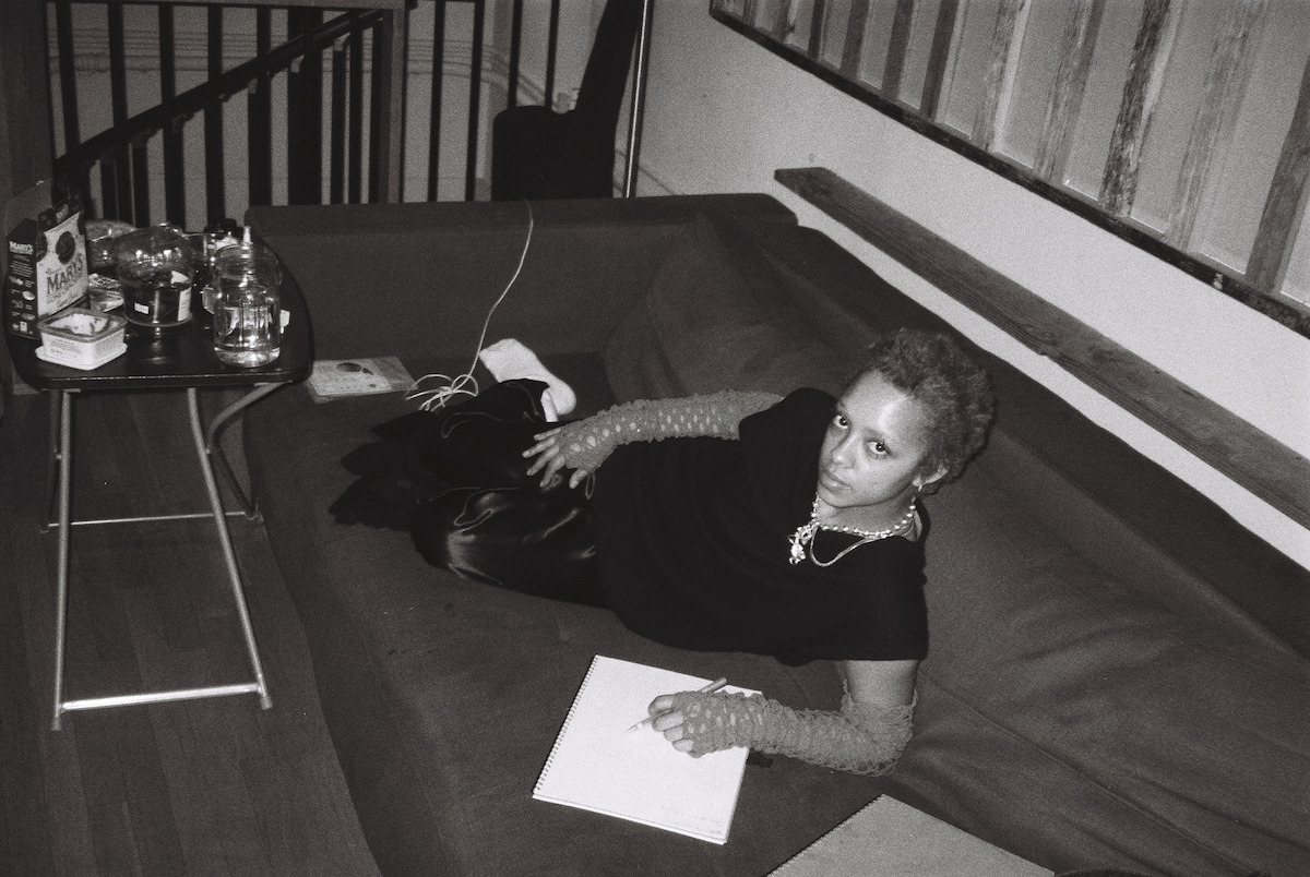 Kelsey Lu lounges on a couch writing on a white pad.