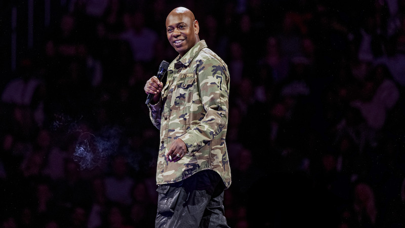 Dave Chappelle on stage holding a microphone.