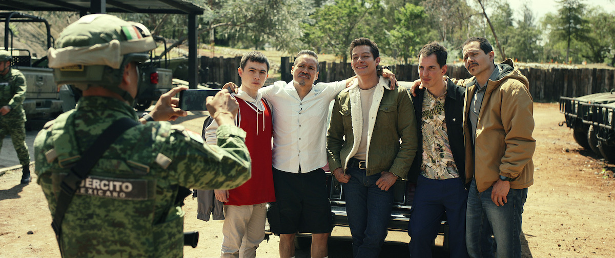 A man in military fatigues takes a photo of a group of men.