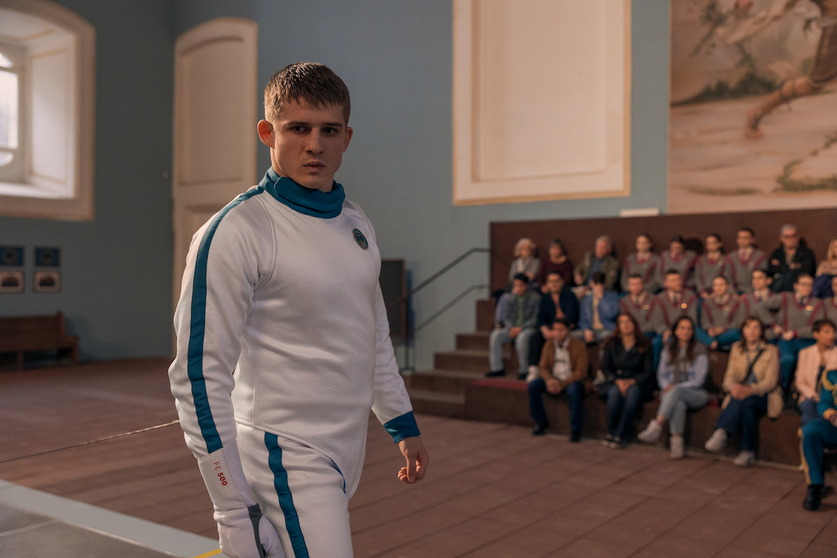 Homem de cabelos curtos e expressão fechada veste trajes de esgrima durante uma prova