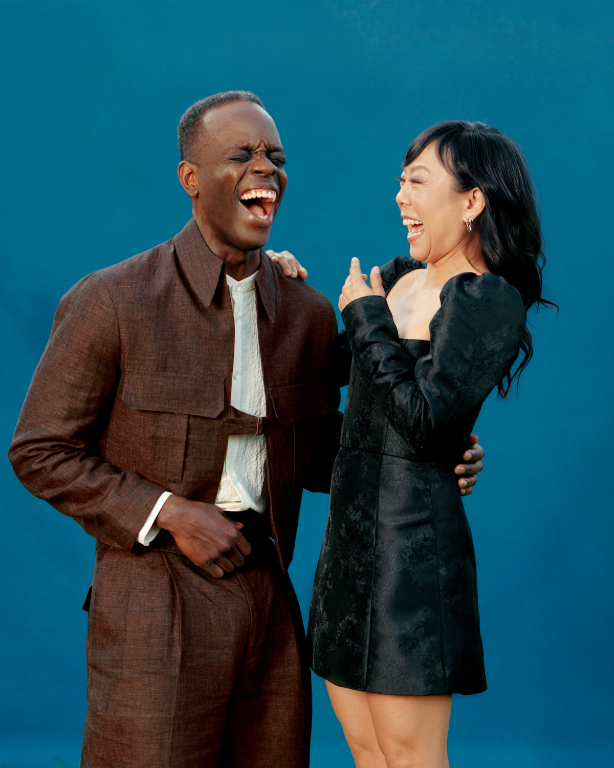 Ato Essandoh and Ali Ahn laughing in front of a blue background.