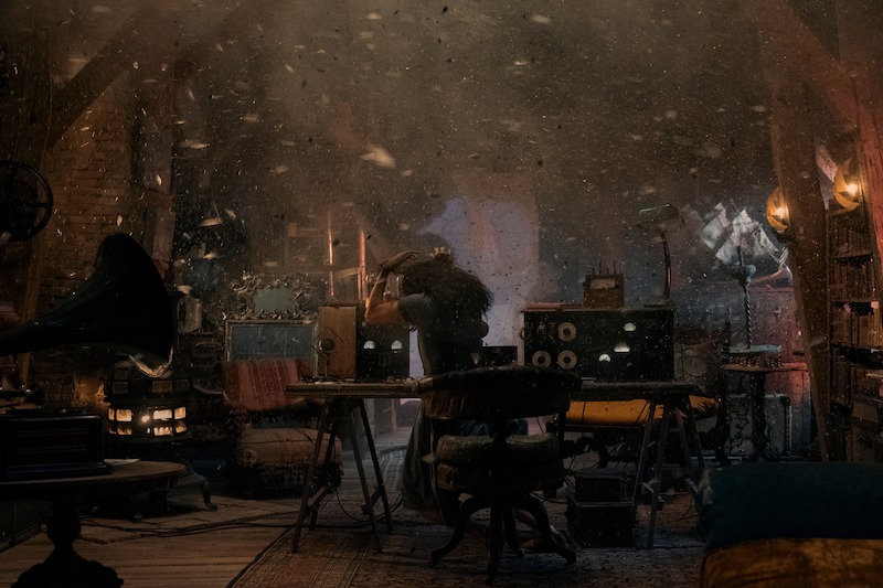 Aria Mia Loberti as Marie-Laure holding her hands up to protect herself from falling debris in an attic. 