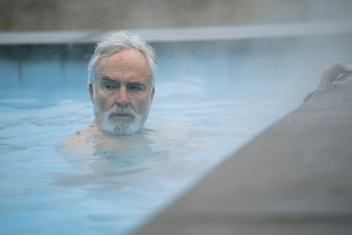 Bradley Whitford as Tom Penn in ‘The Diplomat,’ swims in a steaming pool and looks over his shoulder with a concerned expression.