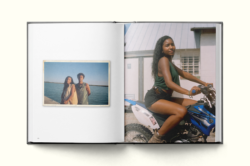 Open photo book showing two images: left page has a vintage-style photo of two people by the water; right page features a woman with long hair sitting confidently on a blue dirt bike outside a building in daylight.