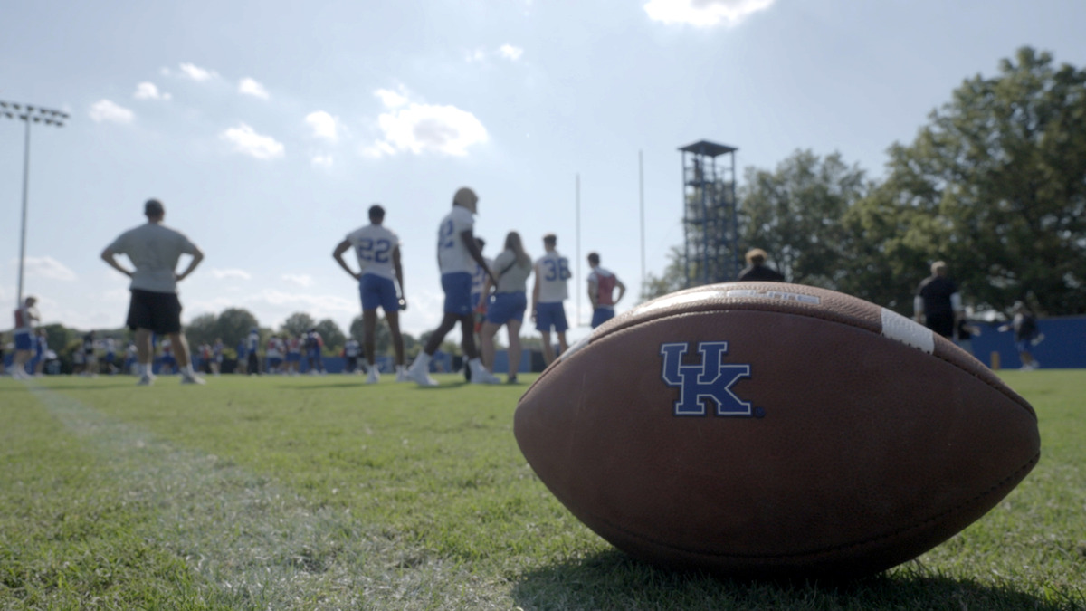 Kentucky Wildcats logo seen on a football in the grass during a practice session.
