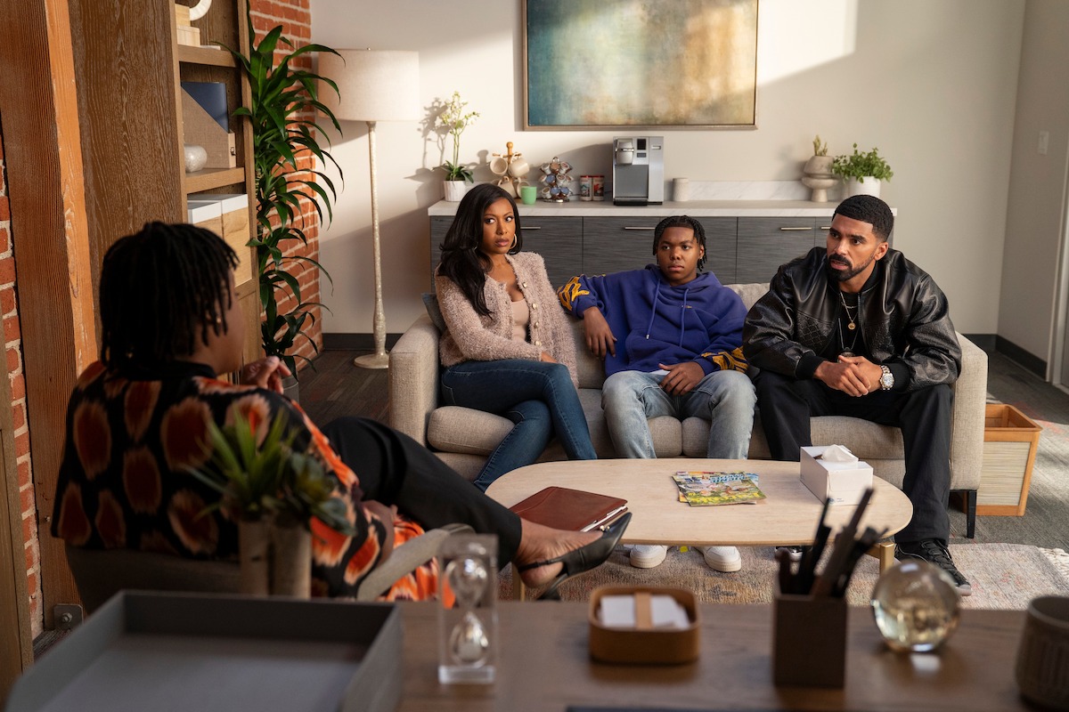 Three people sit on a couch in a cozy, modern office talking to a therapist. Books, plants, and artwork decorate the room, suggesting a professional therapy or counseling session with a relaxed atmosphere.
