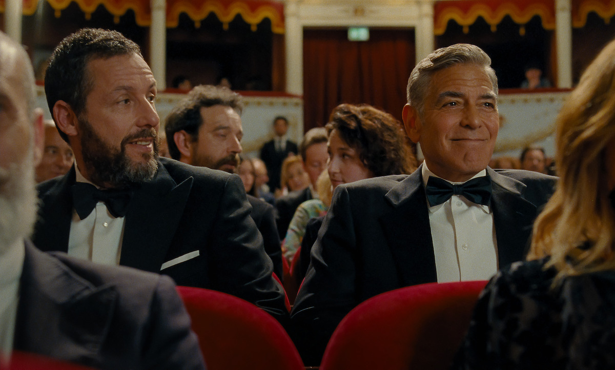 Ron Sukenick (Adam Sandler) and Jay Kelly (George Clooney) sit in a movie theater wearing tuxedos in Italy where a tribute is being made to Jay Kelly’s career.