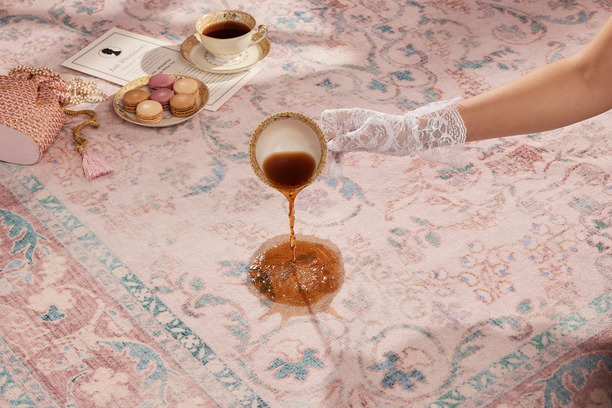 A hand wearing a lace glove spills tea onto a pink and blue rug for the ‘Bridgerton’ collaboration with Ruggable