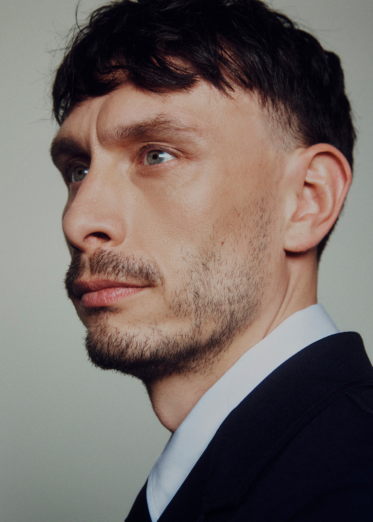 Richard Gadd wears a dark suit and white shirt and looks off into the distance with some scruff on his face.