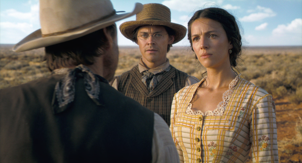 A man faces a woman wearing a yellow dress and a man in a cowboy hat in glasses in ‘Horizon: An American Saga: Chapter 1’