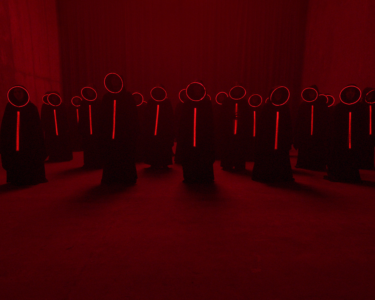 A group of people wear cloaks in a red room in Season 1 of ‘Nightmares and Daydreams.’
