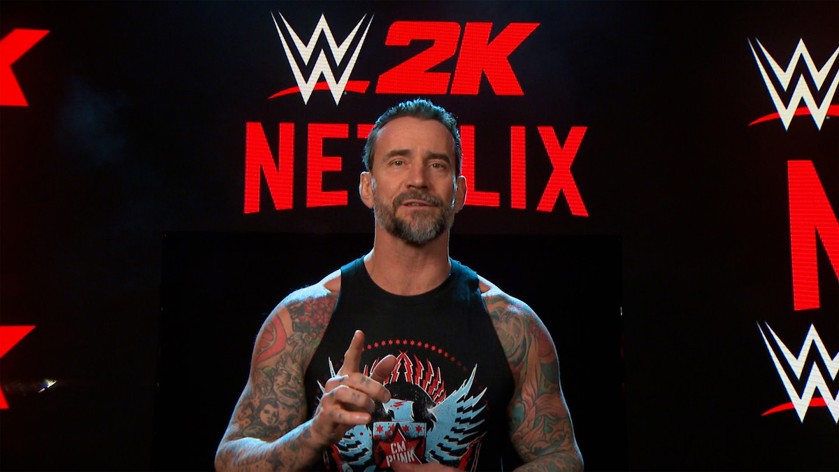 WWE wrestler standing in front of a step and repeat background with Netflix and W2K logos. 