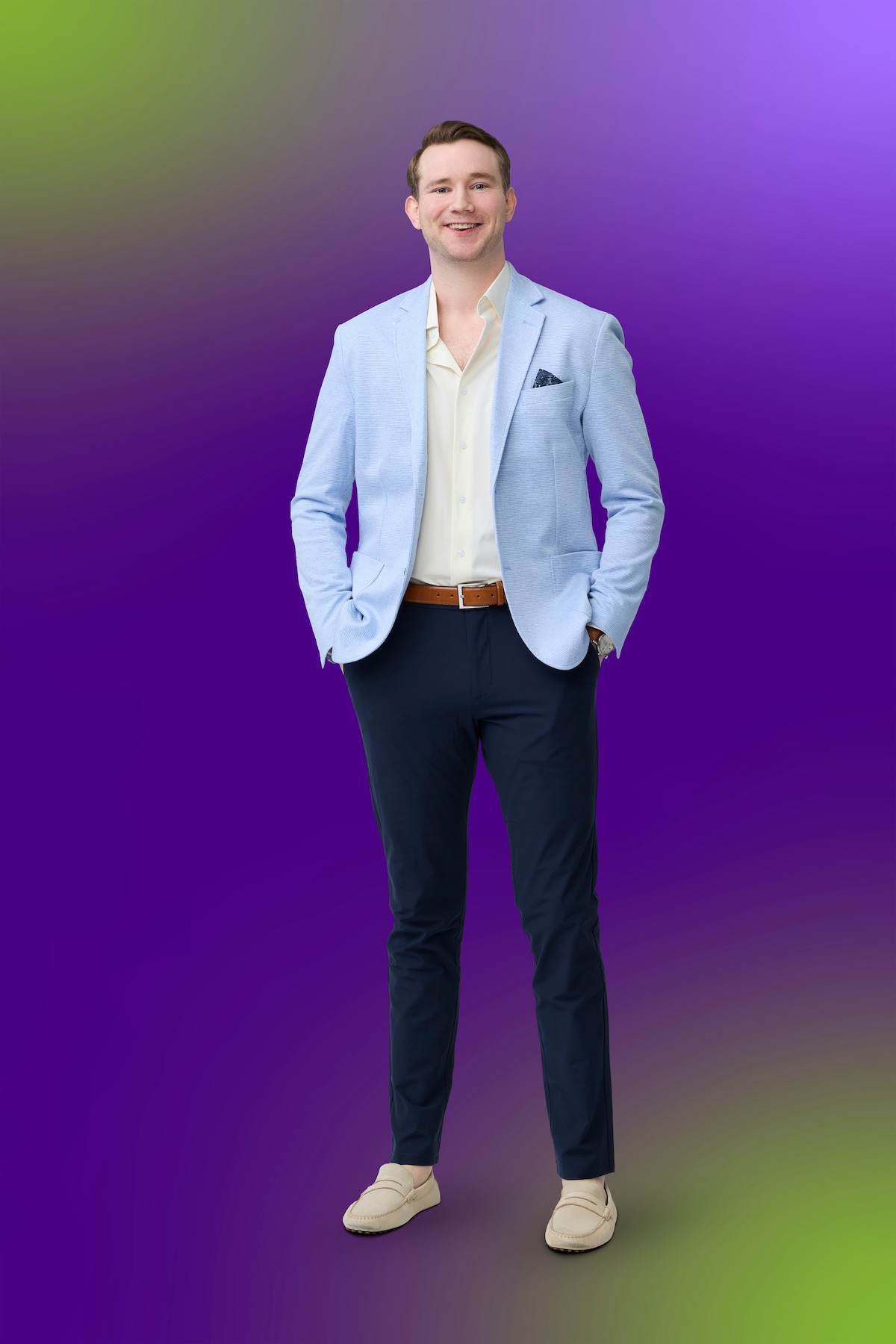 A young man in a light blue blazer, cream shirt, dark pants, and loafers stands confidently with hands in pockets against a gradient purple and green abstract background.A young man in a light blue blazer, cream shirt, dark pants, and loafers stands confidently with hands in pockets against a gradient purple and green abstract background.