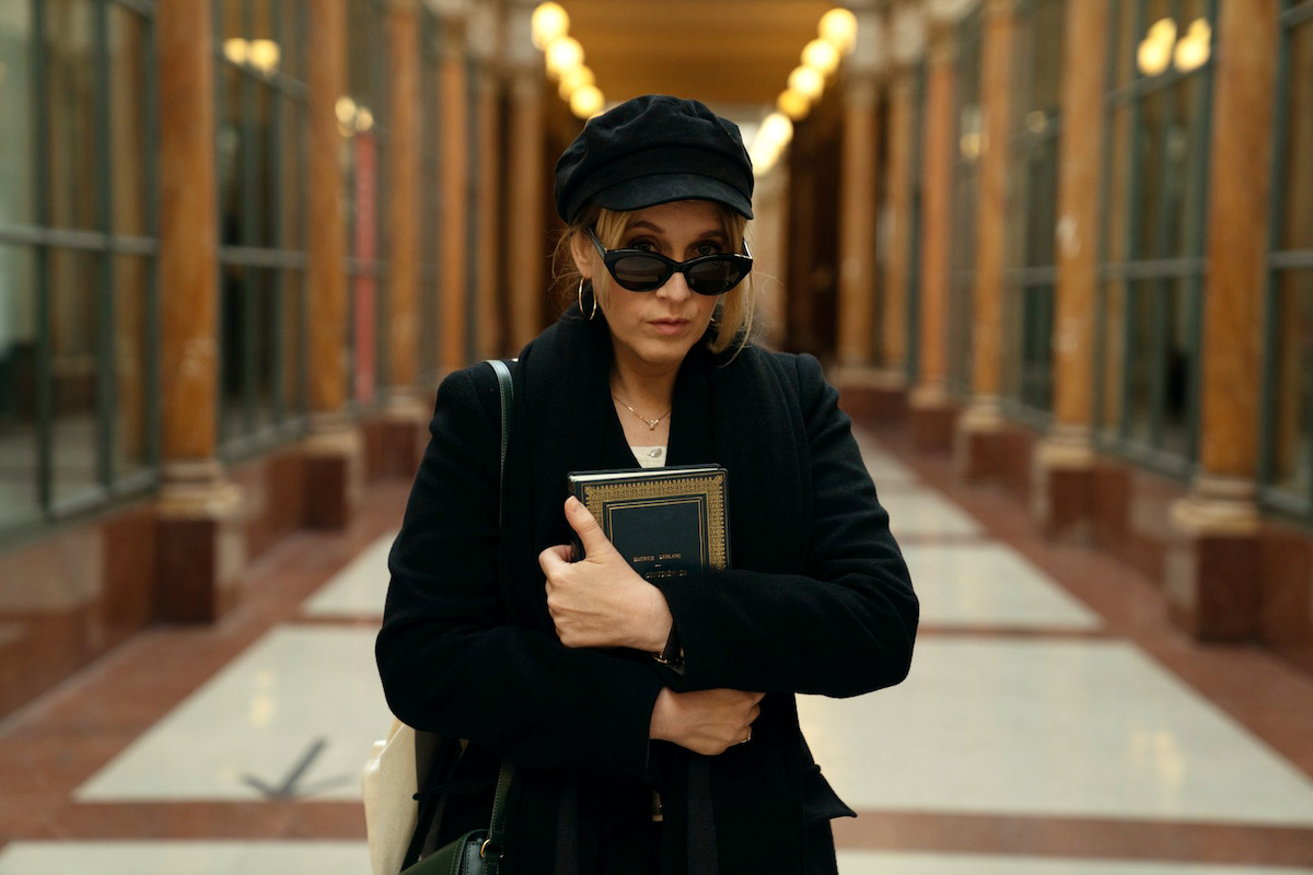 Ludivine Sagnier as Claire walks through a hallway wearing a black hat and sunglasses in Season 3 of ‘Lupin.’