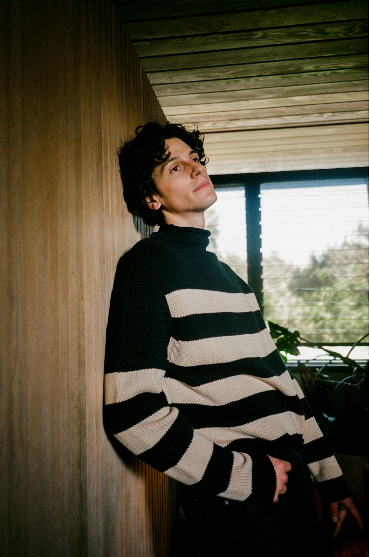 Owen Painter in a black-and-white striped sweater leaning against a wood-paneled wall.