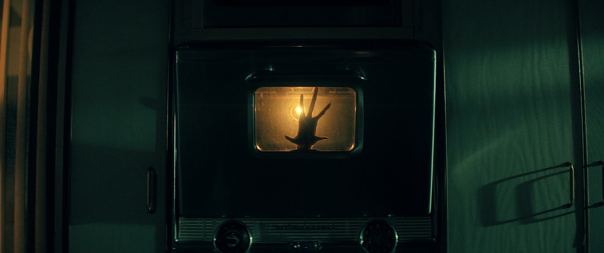 A silhouette of a hand with splayed fingers presses against an oven window in ‘The Boroughs’