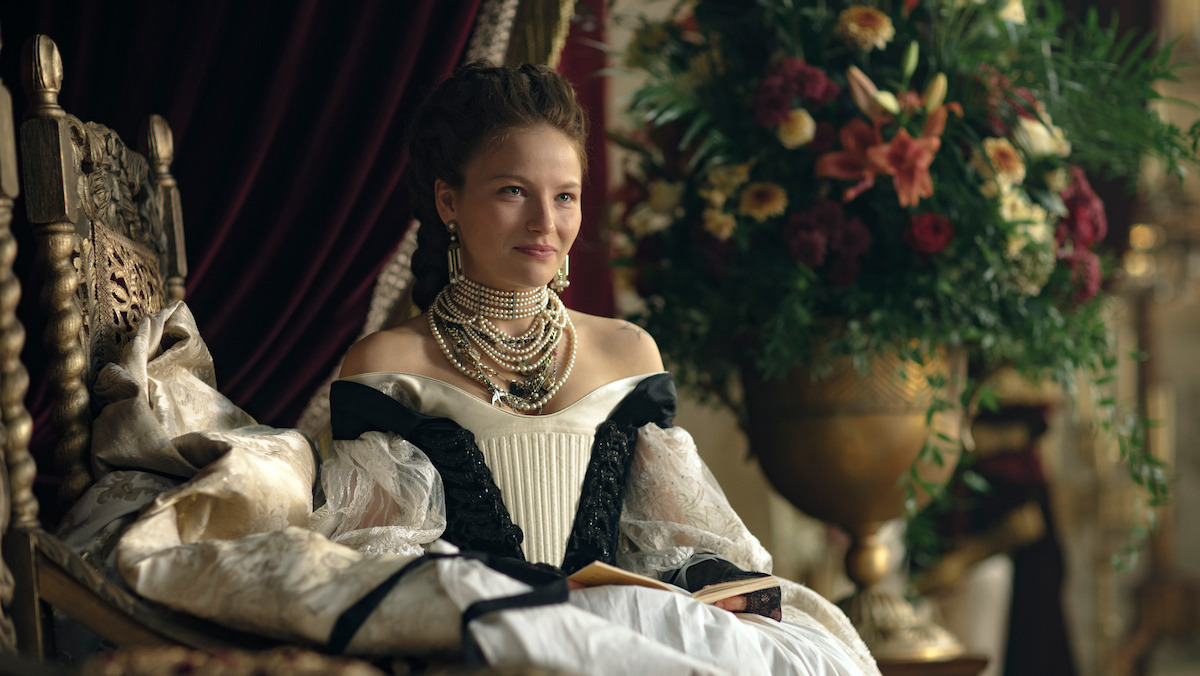 Uma mulher veste trajes de realeza e se senta em um trono na série 'The Empress'