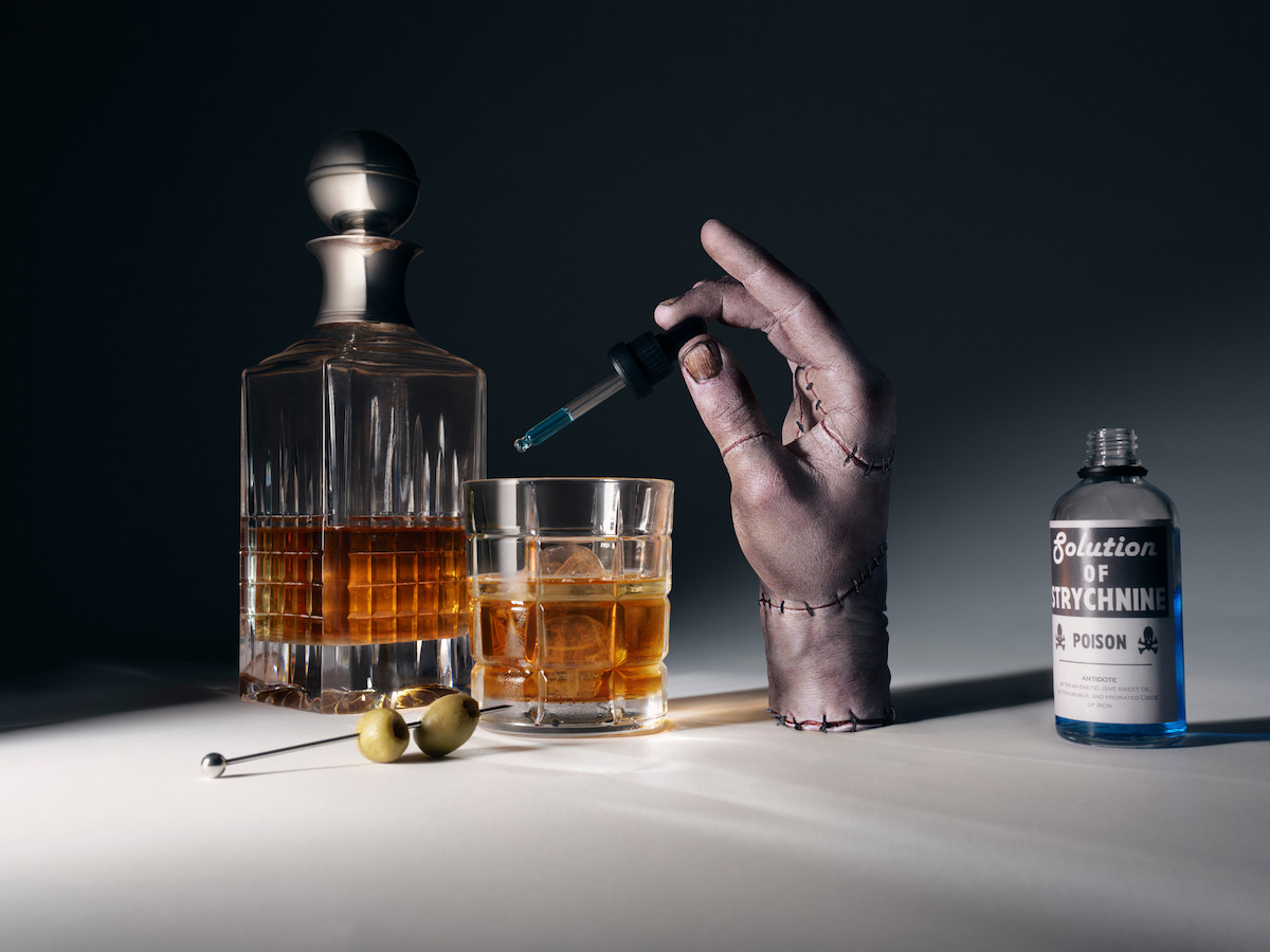 Thing holding a dropper of poision over a glass of whiskey.