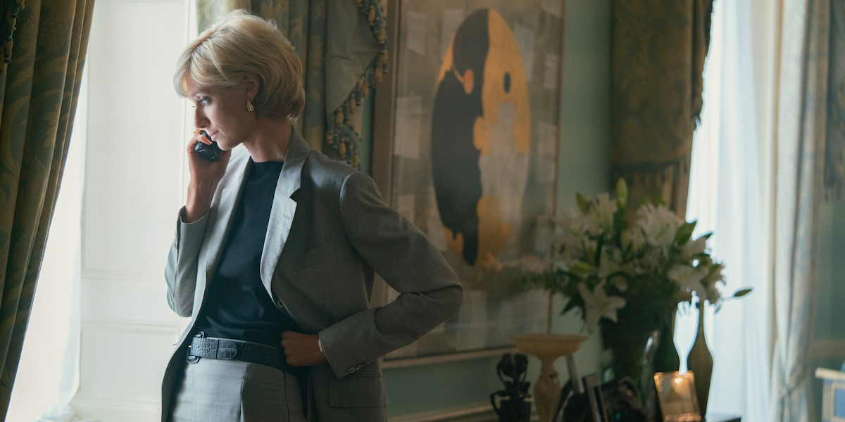 Diana standing in a hotel room on the phone while looking out the window.