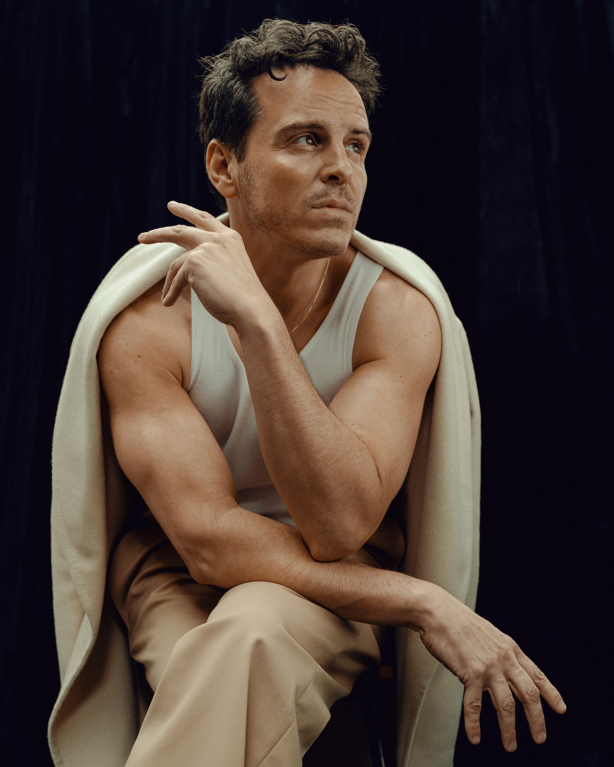 Andrew Scott wears khakis, a white tank, loafers, and a blazer or coat draped over his shoulders.