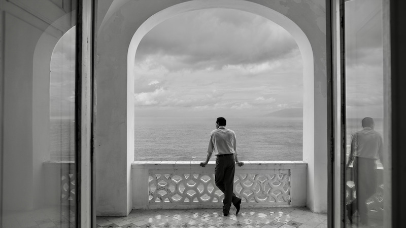 Andrew Scott as Tom Ripley stands on a balcony looking at the ocean in 'Ripley'