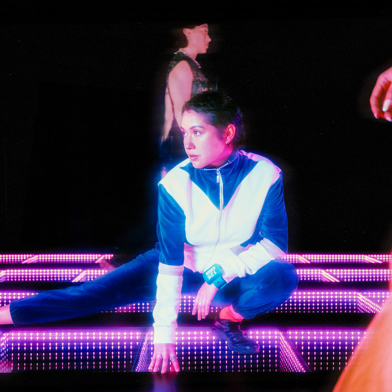A woman in a blue and white jumpsuit squatting on a lit up floor
