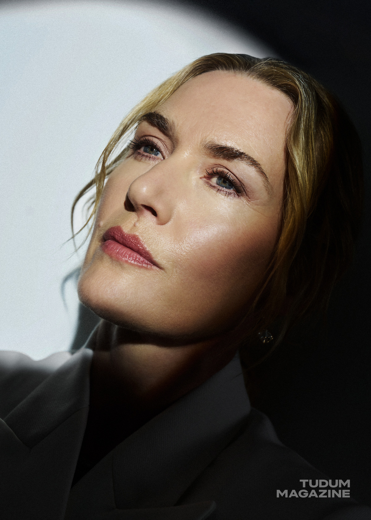 Kate Winslet with a spotlight on her against a white background.