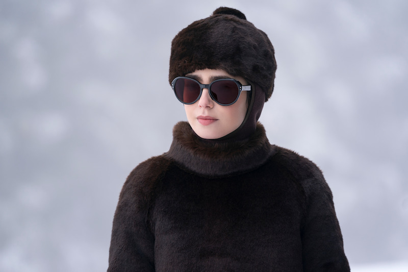 Lily Collins as Emily wears a black coat, hat, and sunglasses in Season 4 of 'Emily in Paris'