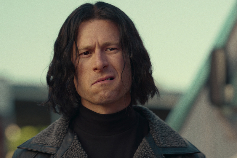 Gary Johnson (Glen Powell) undercover. He wears a leather jacket, black turtleneck, and black bob.