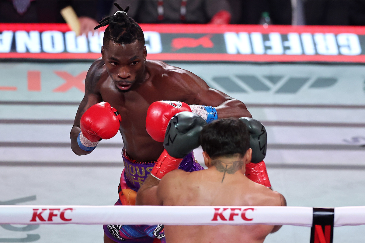 Avious Griffin and Justin Cardona fighting in a boxing ring, wearing gloves and trunks, with a crowd and sponsor logos visible in the background during a professional boxing match.
