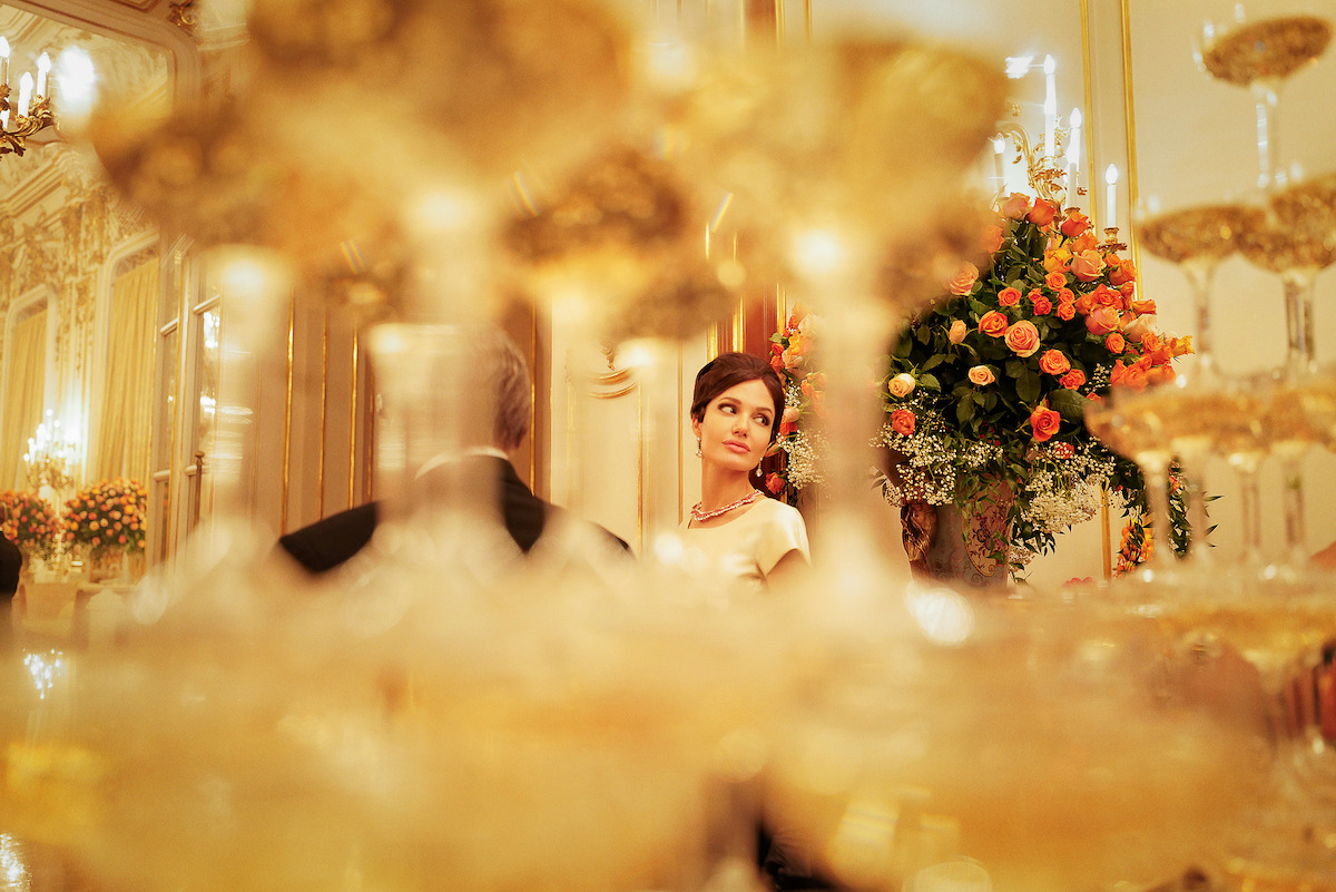 Angelina Jolie as Maria Callas in an opulent ballroom with champagne coupe glass towers.