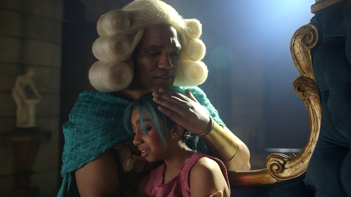 A person in a baroque wig comforts a child with blue hair in a dim, ornate room with stone walls and soft lighting, suggesting a tender, emotional moment in a fantasy or historical setting.