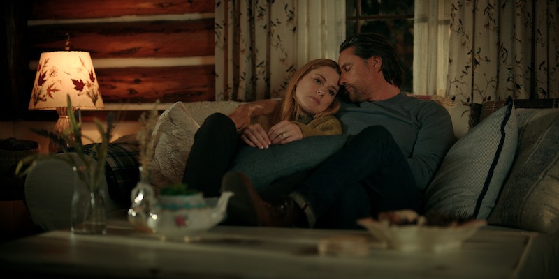 Alexandra Breckenridge as Mel Monroe and Martin Henderson as Jack Sheridan sit together on a couch at night in Season 5 of ‘Virgin River.’
