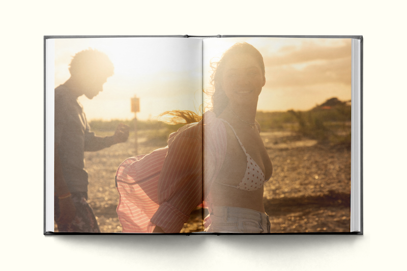 Two people at the beach during sunset, one wearing a bikini top and shirt, the other in shadow, with bright sunlight creating a warm, carefree atmosphere in an open photo book.