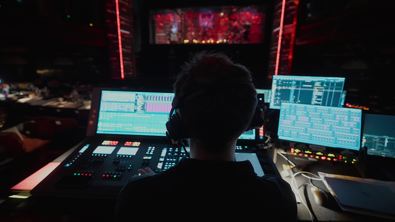A man sits in front of a stage with production equipment around him in 'Behind the Curtain: Stranger Things: The First Shadow'