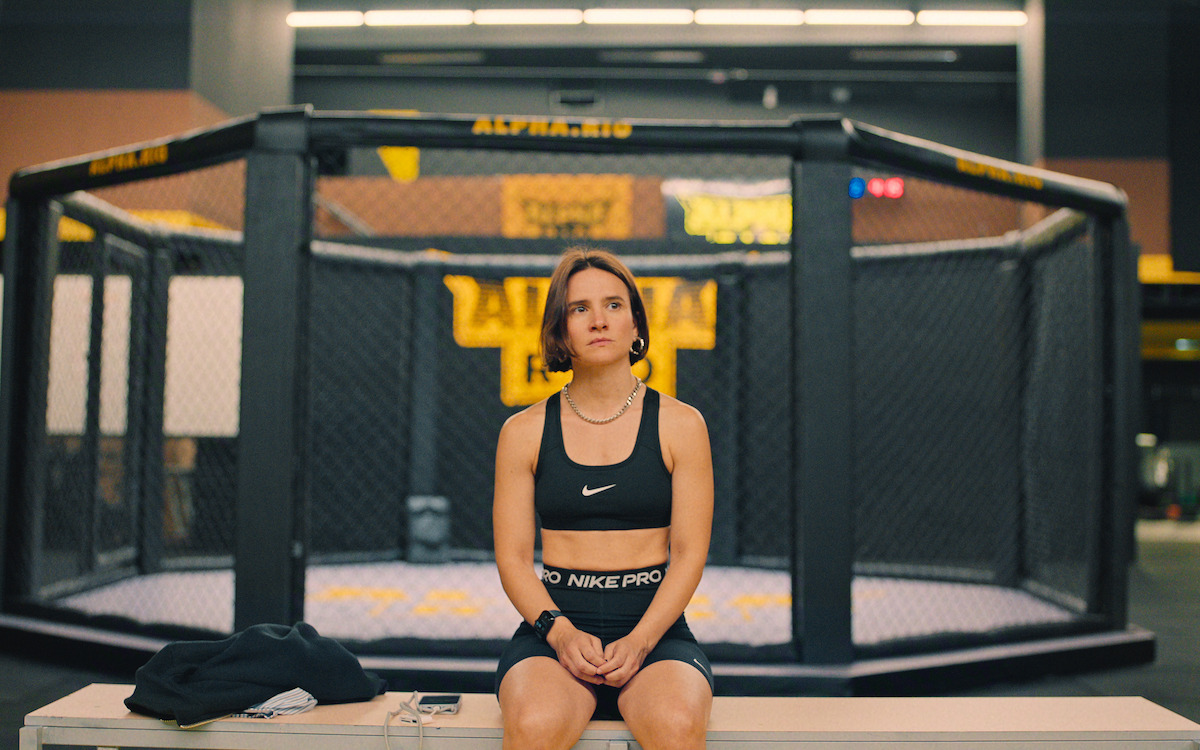 Bianca Comparato descansa em frente a um ring de MMA em cena da série Fúria