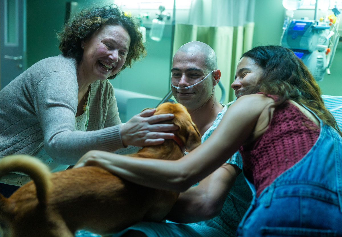 Homem em tratamento oncológico (Rafa Vitti) abraça a família e um cachorro, em cena do filme ‘Caramelo’