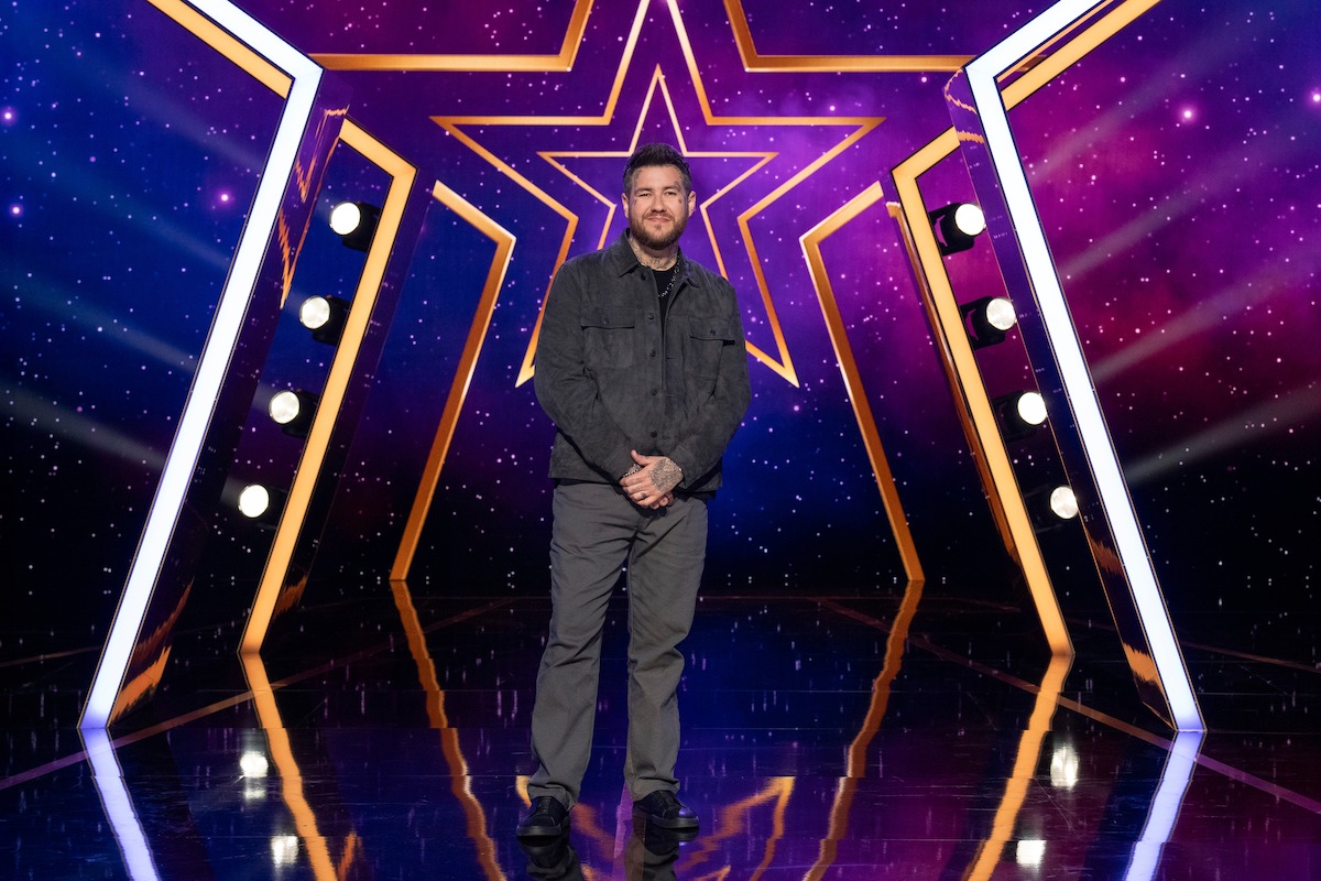 Bear Bailey en un escenario brillante con un gran fondo de estrellas iluminadas y luces de colores violetas y azules, creando una atmósfera vibrante y de espectáculo.