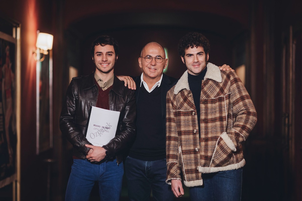 Three men standing together, one holding a script. 
