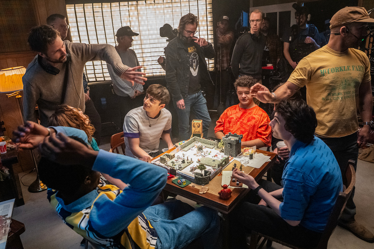 A film crew surrounds teens playing a detailed tabletop fantasy game, directing the scene around the crowded gaming table.