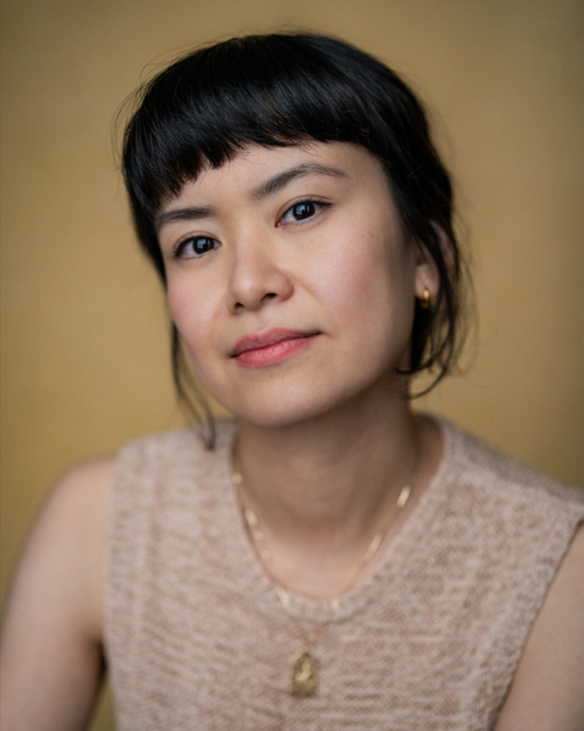 Katie Leung smiles and wears a beige vest.