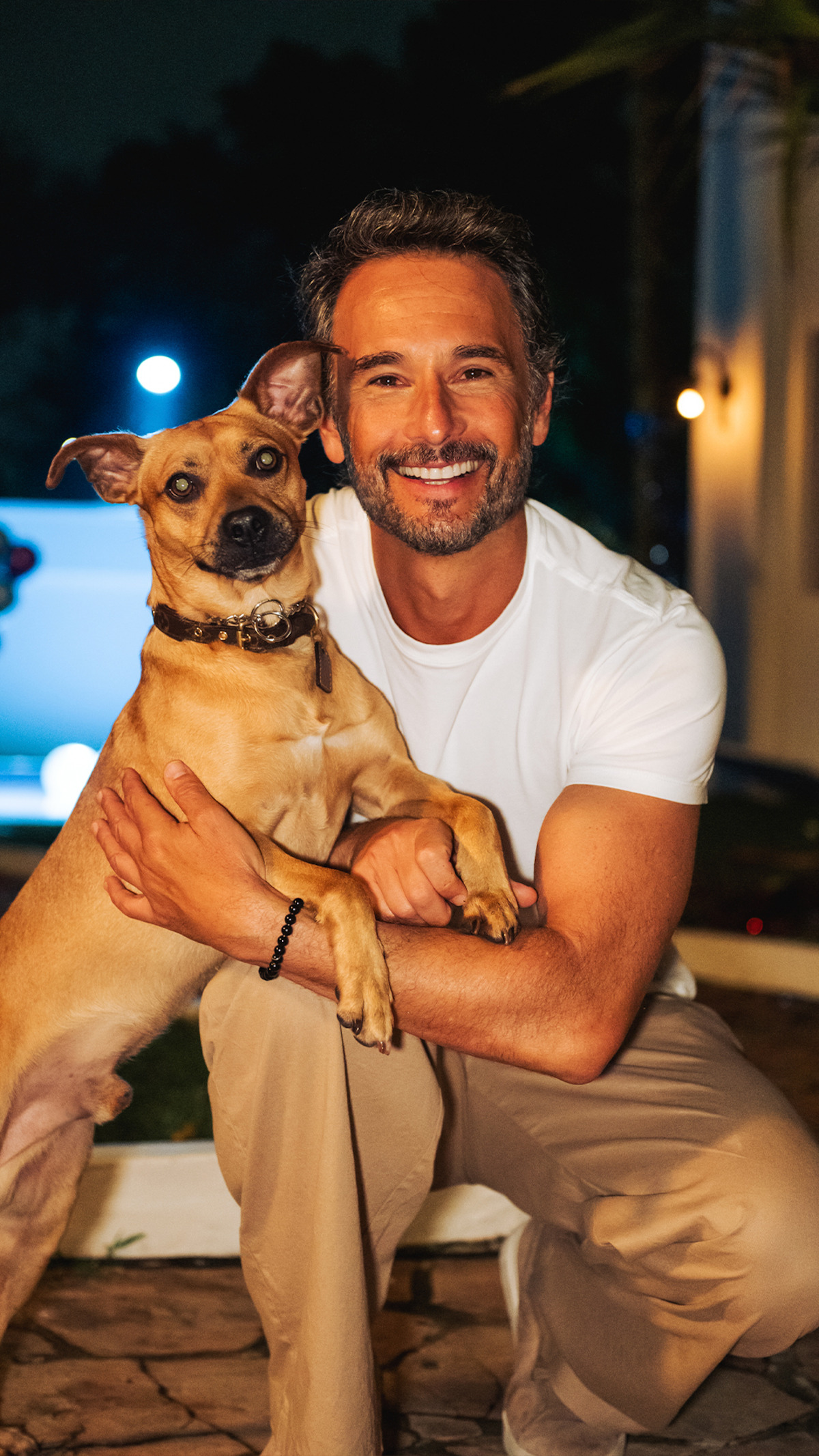 Rodrigo Santoro e o cachorro caramelo se abraçam em uma área externa de piscina