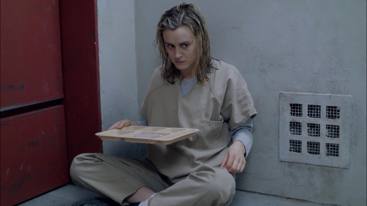 Piper sitting on the floor of the jail, holding a tray. 