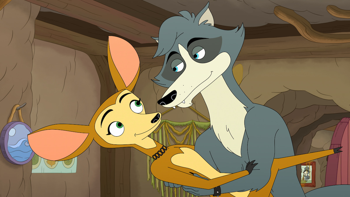 Animated wolf and antelope characters sharing a tender moment in a cozy, cave-like room with earthy walls, wooden beams, hanging drapes, and wall decorations in the background.