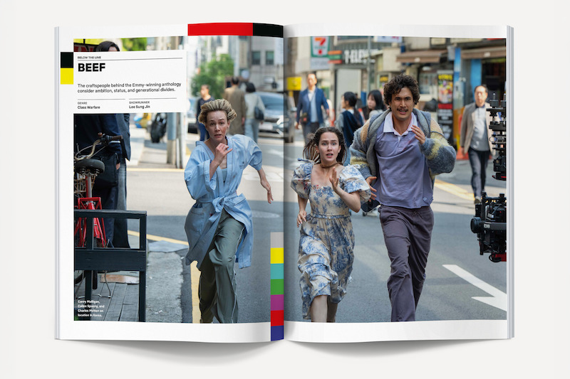Two women and a man in urban clothing run down a busy city street while a film camera crew follows; people, vehicles, and buildings fill the lively background.