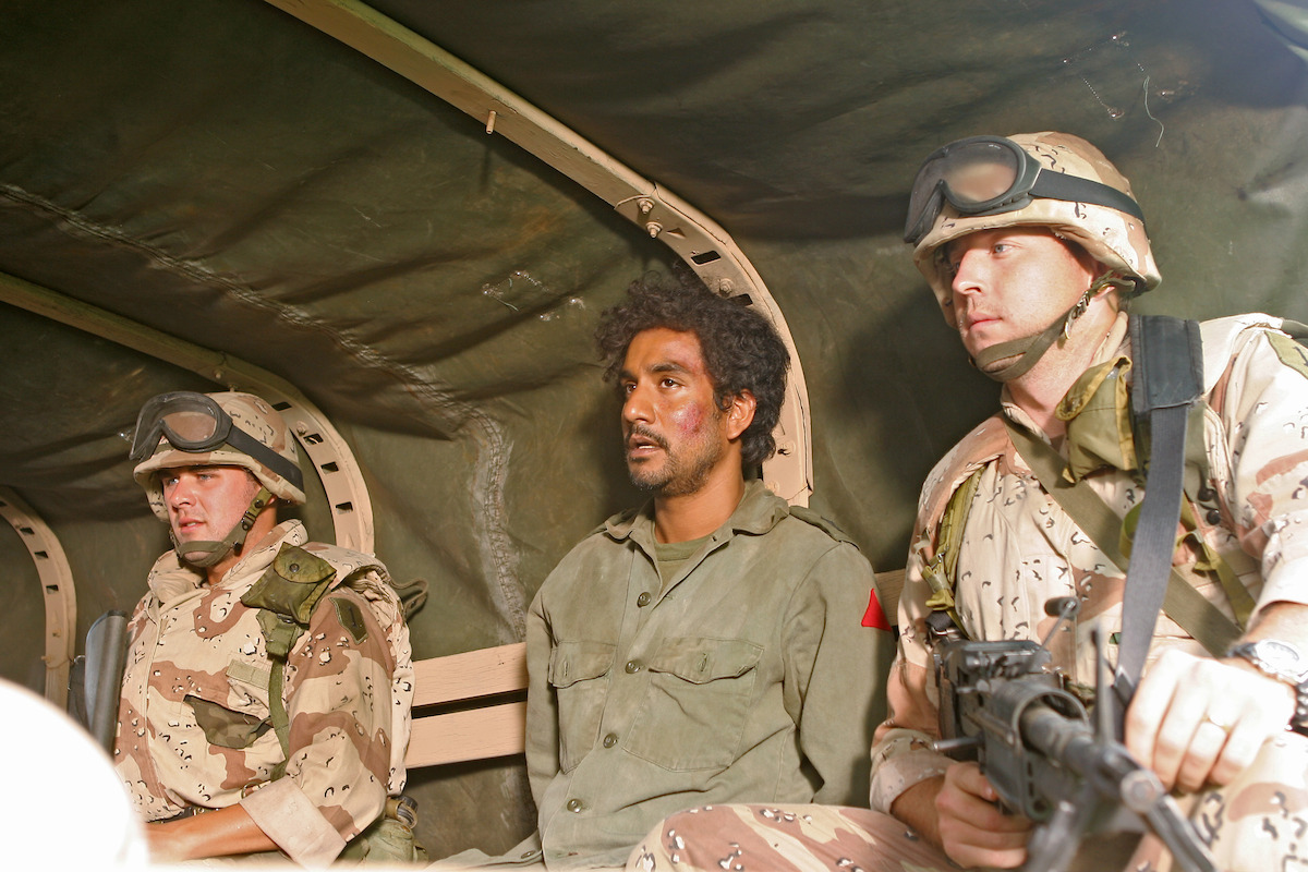 Naveen Andrews is transported by soldiers in a truck.