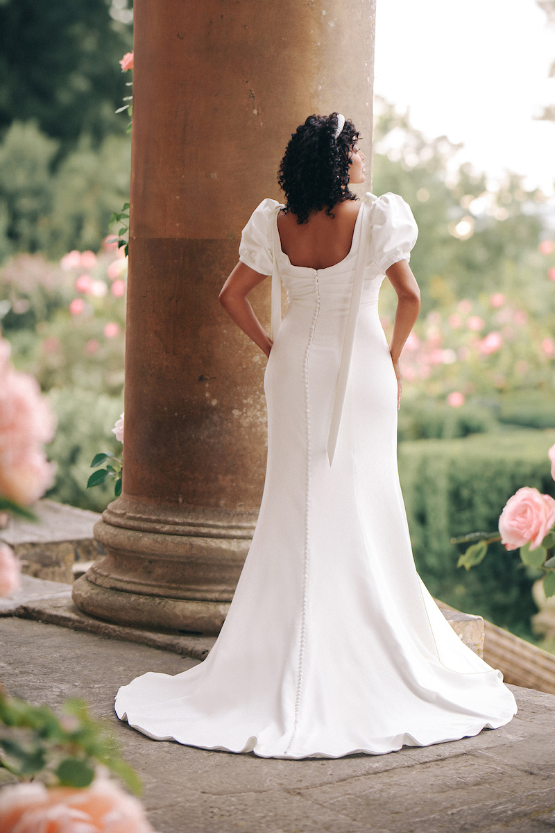 Woman in bridal dresses poses and looks off into the distance.
